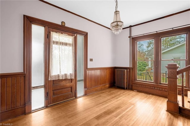 doorway to outside featuring an inviting chandelier, radiator, crown molding, and light wood-type flooring