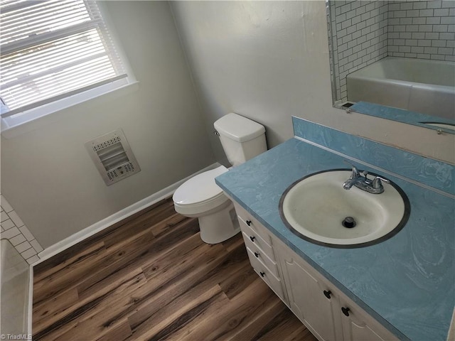 bathroom with vanity, heating unit, hardwood / wood-style floors, toilet, and a bathing tub