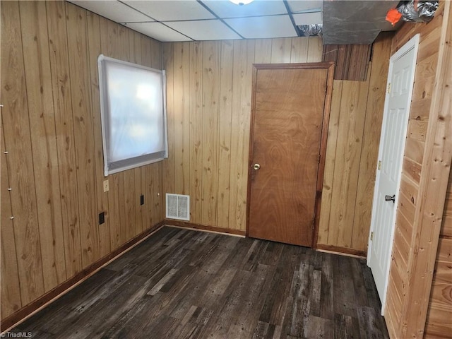 spare room featuring a paneled ceiling, wooden walls, and dark wood-type flooring