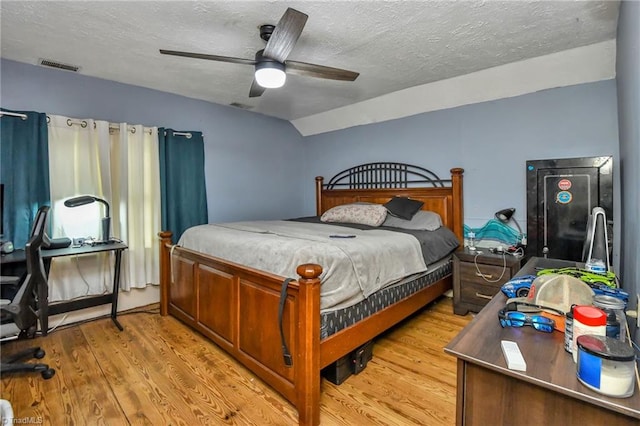 bedroom with a textured ceiling, light wood-type flooring, vaulted ceiling, and ceiling fan