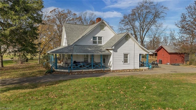 rear view of property featuring covered porch, an outbuilding, and a lawn