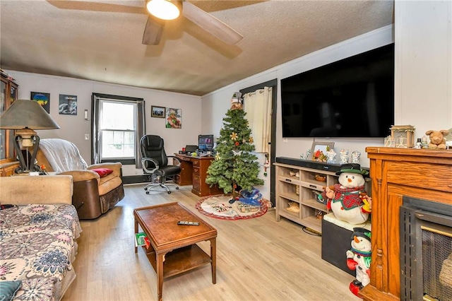 living room with ceiling fan, ornamental molding, a textured ceiling, and light wood-type flooring