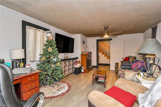 living room featuring ceiling fan, a fireplace, a textured ceiling, and light wood-type flooring