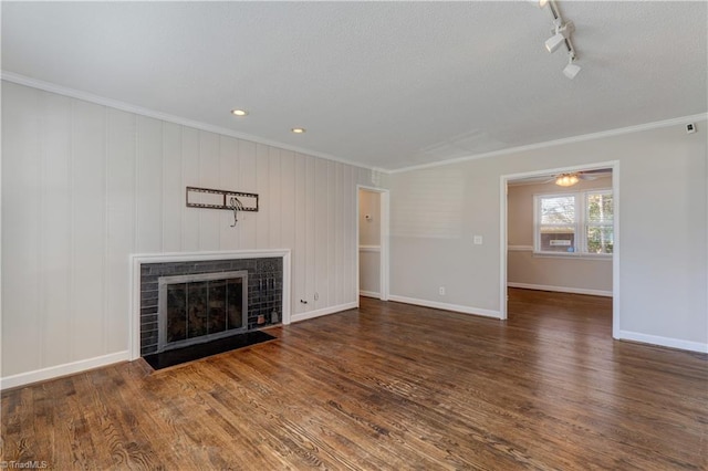 unfurnished living room with ceiling fan, a fireplace, dark wood-type flooring, ornamental molding, and rail lighting