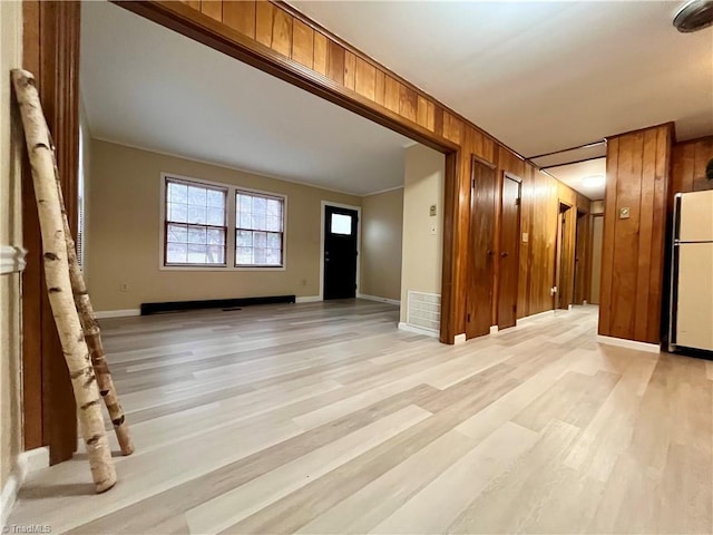 interior space with light wood-type flooring, wooden walls, and baseboards