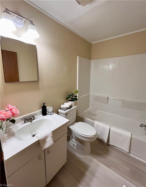 bathroom with toilet, shower / tub combination, wood finished floors, crown molding, and vanity