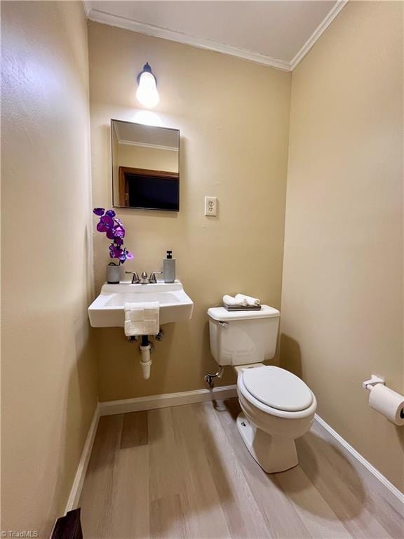 bathroom with toilet, baseboards, wood finished floors, and ornamental molding