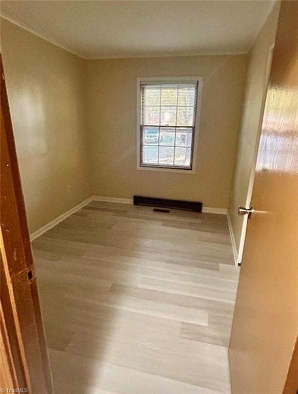 spare room with light wood-type flooring, visible vents, and baseboards