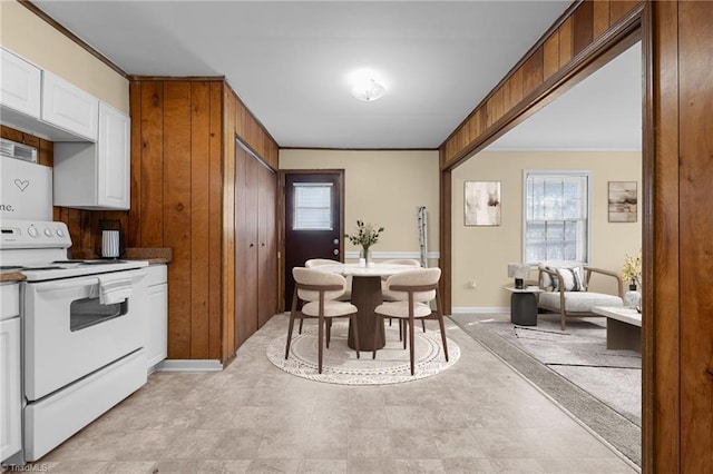 kitchen featuring wooden walls, baseboards, white cabinets, crown molding, and white range with electric cooktop