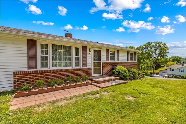 view of front of property featuring brick siding, a front yard, and a chimney