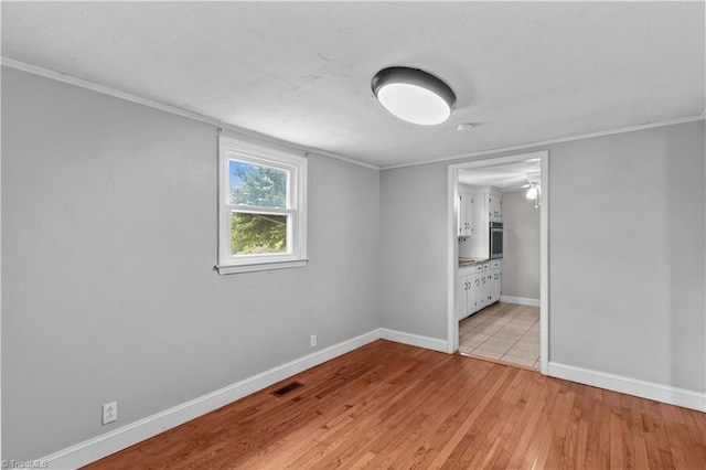 unfurnished bedroom with light wood-style floors, baseboards, crown molding, and ensuite bath