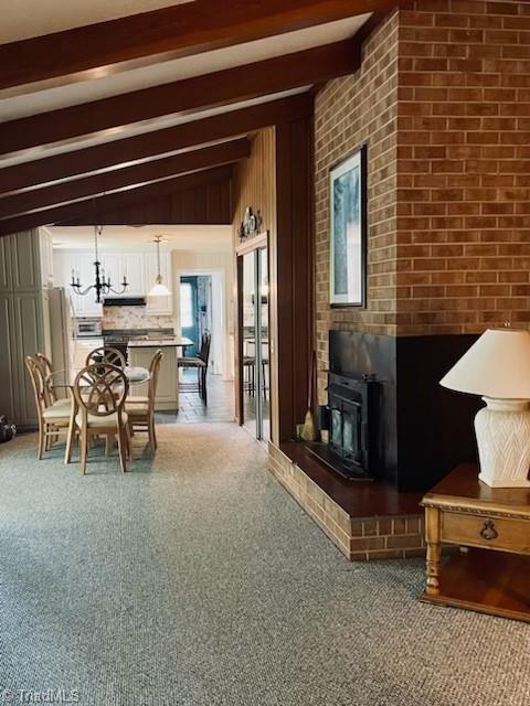 carpeted living room featuring lofted ceiling with beams, a wood stove, and an inviting chandelier