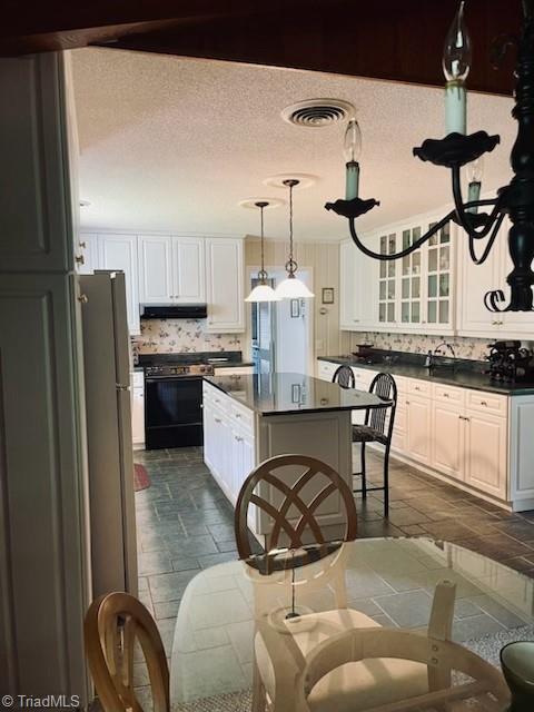 kitchen featuring pendant lighting, backsplash, gas stove, white cabinets, and a kitchen island