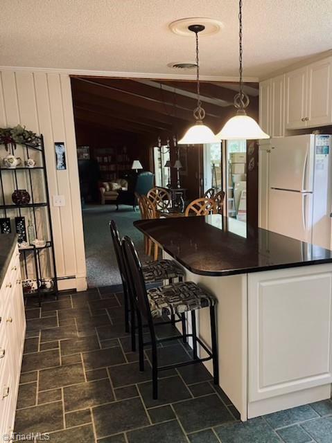 kitchen featuring a textured ceiling, hanging light fixtures, white fridge, and white cabinets