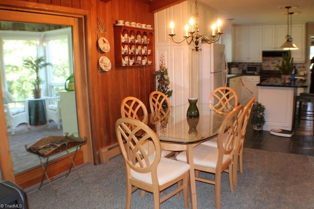 dining area featuring an inviting chandelier, dark carpet, baseboard heating, and wood walls