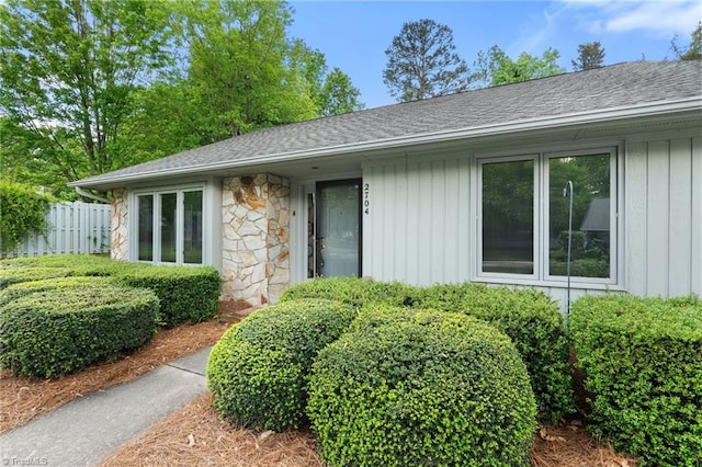 exterior space featuring fence, board and batten siding, roof with shingles, and stone siding