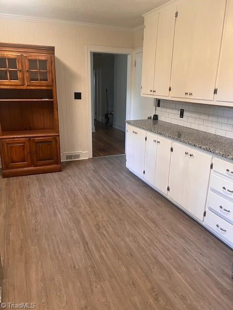 kitchen with ornamental molding, white cabinetry, dark stone counters, and dark hardwood / wood-style flooring