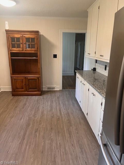 kitchen featuring dark stone countertops, crown molding, white cabinetry, stainless steel refrigerator, and dark hardwood / wood-style flooring