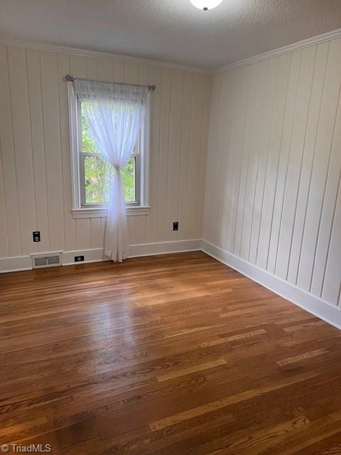 unfurnished room featuring crown molding, wood-type flooring, a textured ceiling, and wooden walls