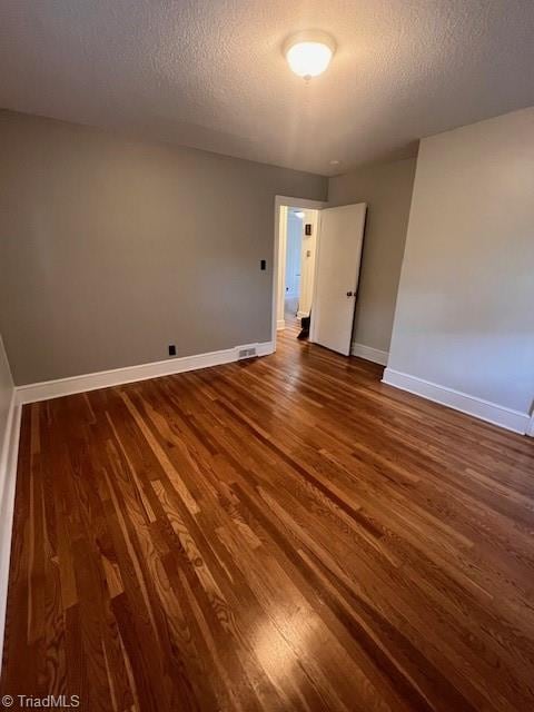 unfurnished room featuring a textured ceiling and dark hardwood / wood-style flooring