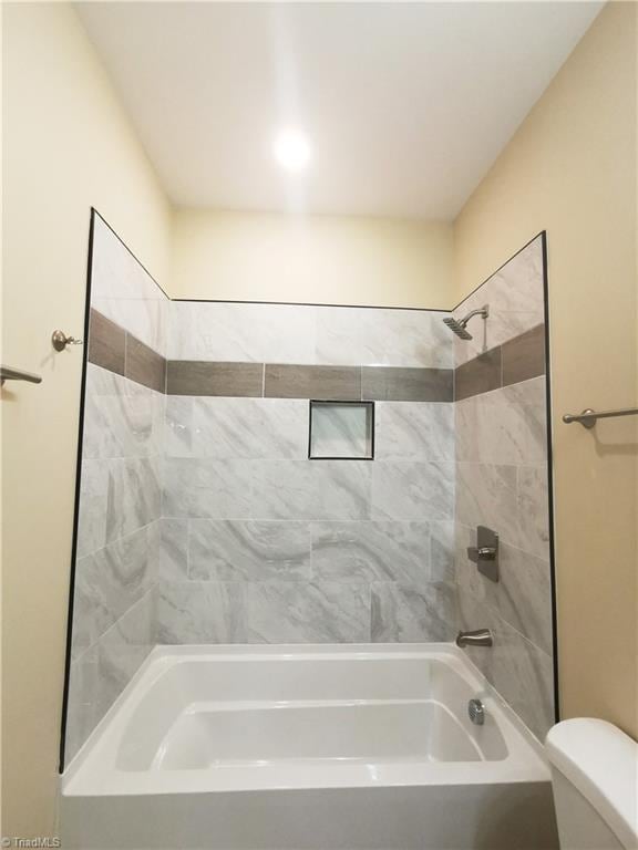 bathroom with toilet and tiled shower / bath