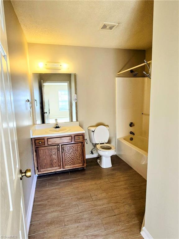 full bathroom with hardwood / wood-style floors, vanity, shower / bathing tub combination, a textured ceiling, and toilet