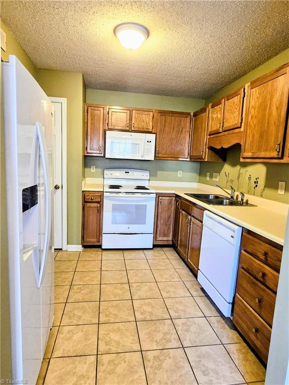 kitchen with sink, light tile patterned floors, a textured ceiling, and white appliances