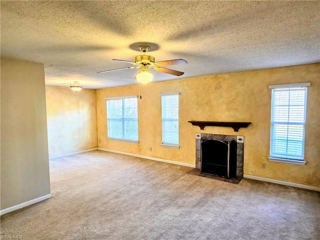 unfurnished living room with a tiled fireplace, carpet floors, a wealth of natural light, and ceiling fan