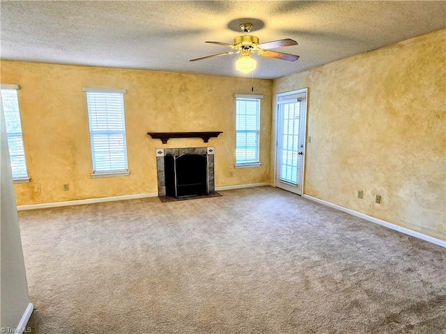 unfurnished living room with a tile fireplace, carpet flooring, a wealth of natural light, and a textured ceiling