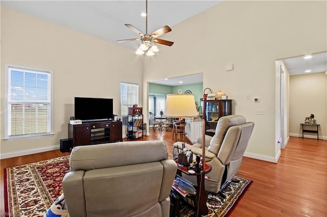 living room featuring a towering ceiling, wood-type flooring, and ceiling fan