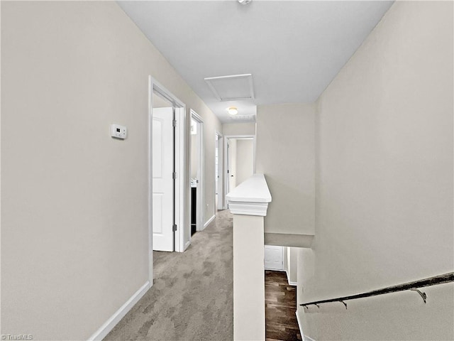 hallway featuring an upstairs landing, attic access, baseboards, and carpet floors