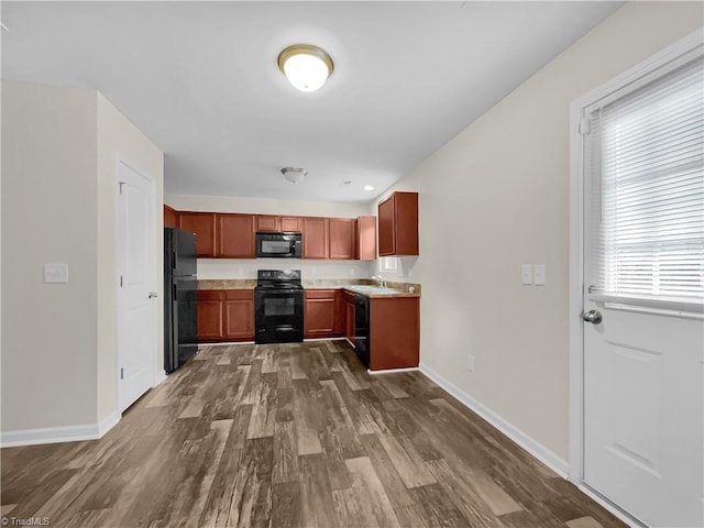 kitchen with baseboards, light countertops, dark wood-style flooring, black appliances, and a sink