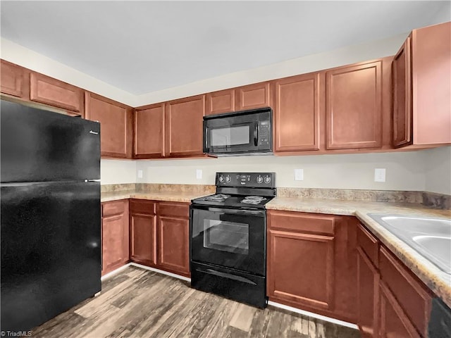 kitchen featuring light countertops, wood finished floors, brown cabinetry, black appliances, and a sink