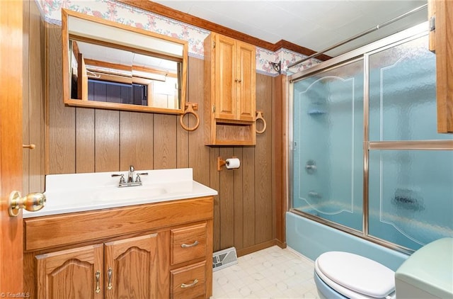 full bathroom with vanity, combined bath / shower with glass door, toilet, and wooden walls