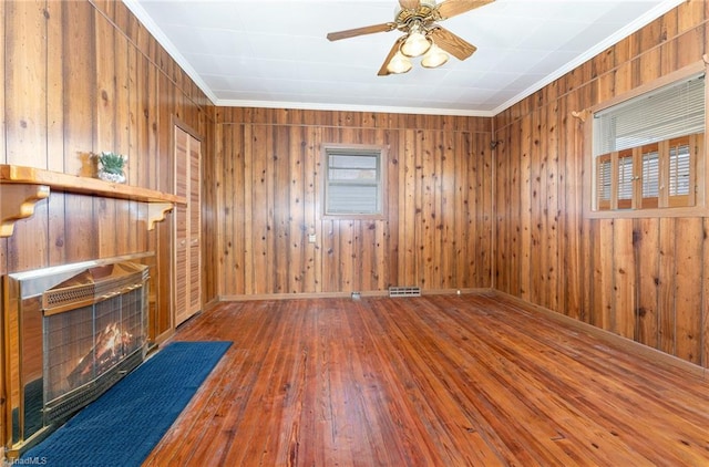 unfurnished living room featuring wooden walls, ceiling fan, wood-type flooring, and ornamental molding