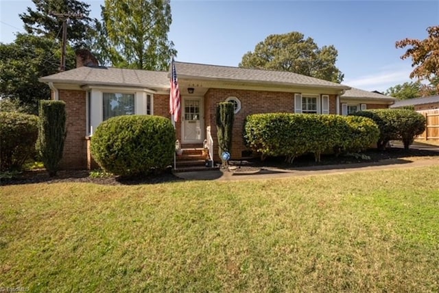 single story home with entry steps, brick siding, a chimney, and a front yard