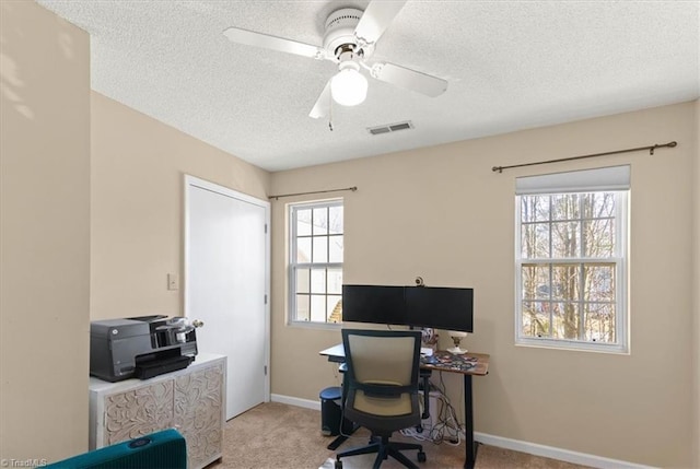 office space with light colored carpet, visible vents, a ceiling fan, a textured ceiling, and baseboards