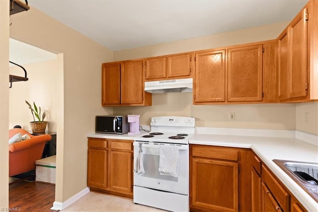 kitchen with light countertops, electric range, brown cabinets, and under cabinet range hood