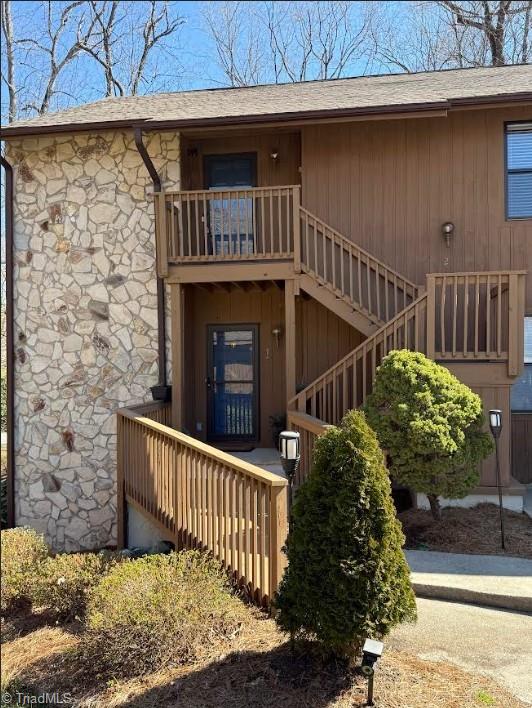 entrance to property with a balcony, stone siding, and a shingled roof