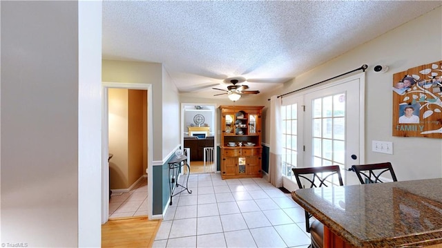 dining space with light tile patterned flooring, a ceiling fan, french doors, and a textured ceiling