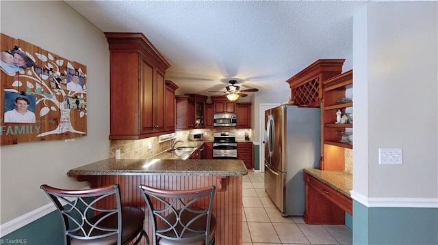 kitchen featuring decorative backsplash, appliances with stainless steel finishes, ceiling fan, a sink, and a peninsula
