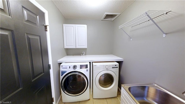laundry room featuring a sink, cabinet space, washer and clothes dryer, light tile patterned floors, and a textured ceiling