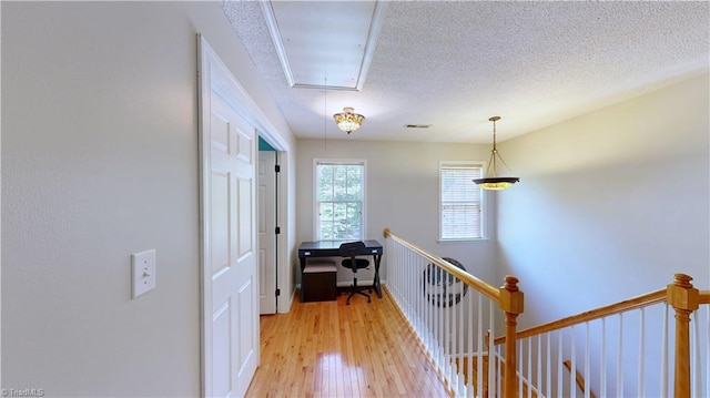 hall with an upstairs landing, attic access, light wood-style flooring, and a textured ceiling