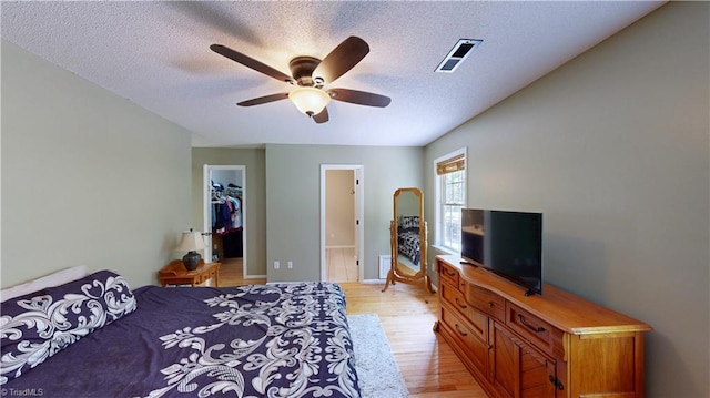 bedroom with a textured ceiling, visible vents, a spacious closet, and light wood-style flooring