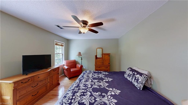 bedroom featuring a textured ceiling, visible vents, ceiling fan, and light wood-style floors