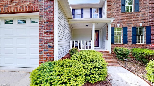 entrance to property featuring a garage, brick siding, and a porch