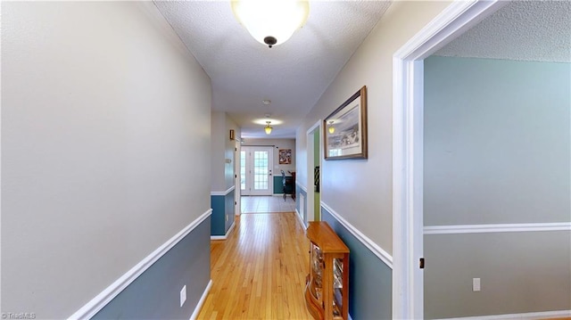 hall featuring baseboards, a textured ceiling, french doors, and light wood finished floors