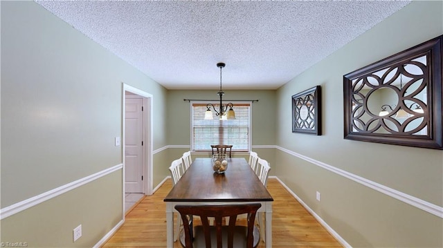 dining area featuring a textured ceiling, an inviting chandelier, baseboards, and light wood-style floors