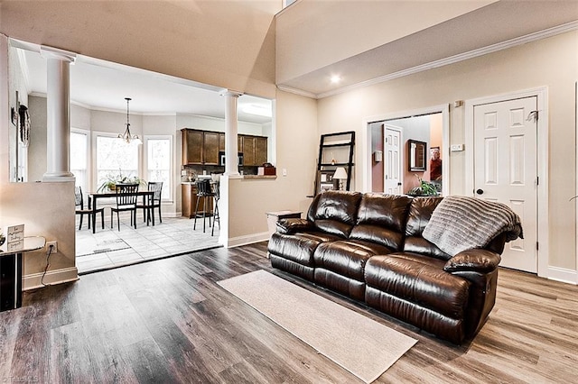 living room featuring decorative columns, ornamental molding, a chandelier, and light wood-type flooring