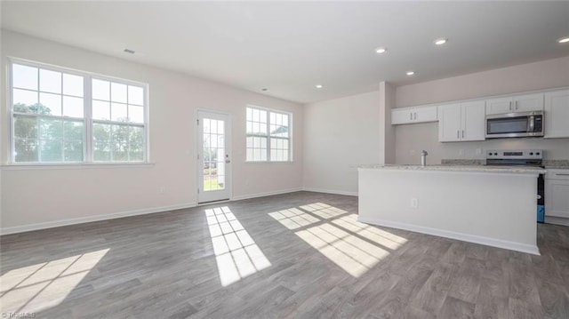 kitchen with white cabinetry, stove, light stone counters, an island with sink, and light wood-type flooring